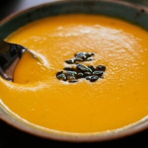 Close-up of creamy pumpkin soup with seeds in a blue ceramic bowl, perfect for a warm fall meal.
